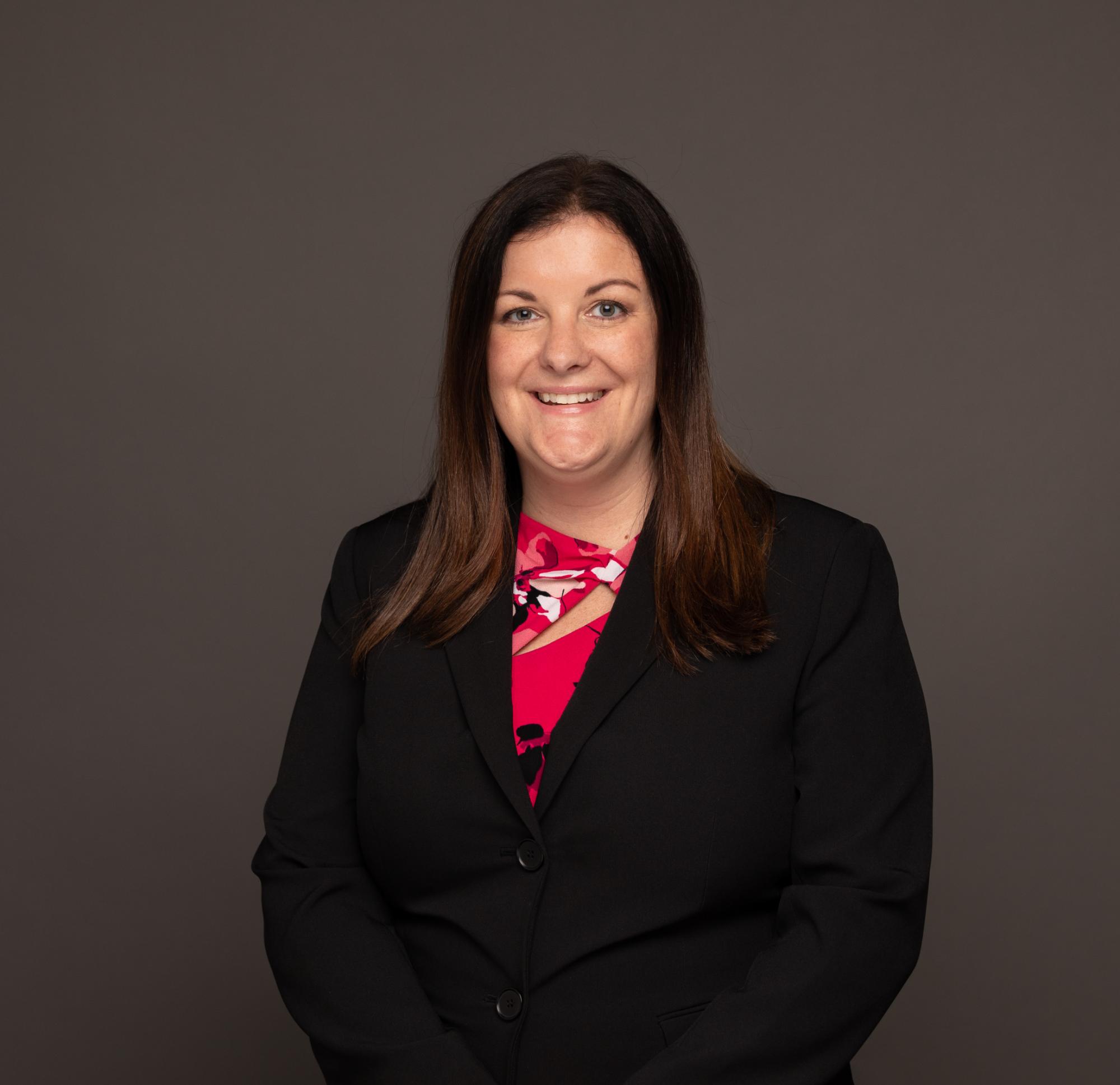 A formal headshot of Julie Mattox wearing a black blazer and a shirt with red flowers
